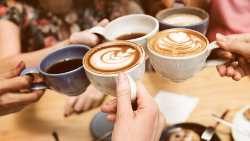 Friends clinking mugs of handcrafted lattes and black coffee—celebrating the everyday joy of great coffee and good company